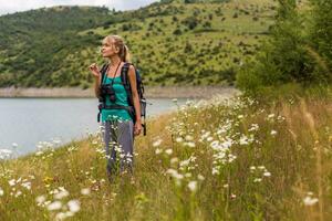 Frau Wanderer genießt riechen Blume während Stehen im das schön Natur. foto