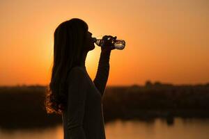 Silhouette von ein Frau Trinken Wasser beim das Sonnenuntergang. foto