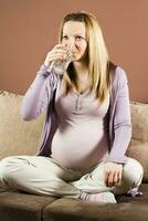 schwanger Frau Sitzung auf das Sofa und Trinken Wasser foto