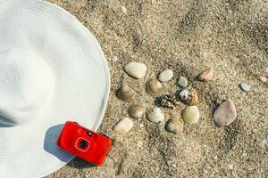 Weiß Hut, ein rot Kamera und Muscheln auf das Sand foto