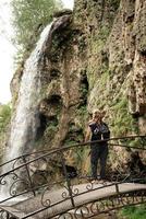 Frau, die auf der Brücke steht und den schönen Bergwasserfall betrachtet foto