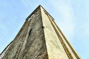 das hoch Backstein Turm von ein Kirche gegen ein Blau Himmel foto