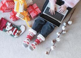 junge Frau in Weihnachtsmütze online einkaufen umgeben von Geschenken Draufsicht flach foto