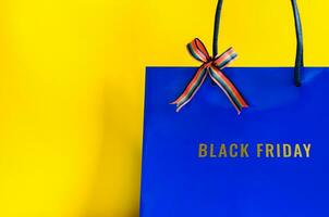 Blau Einkaufen Tasche mit Band und schwarz Freitag Wort auf Gelb Hintergrund zum schwarz Freitag Einkaufen Konzept. foto