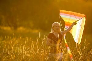 glücklich jung Frau Laufen mit ein Drachen auf ein Lichtung beim Sonnenuntergang im Sommer- foto