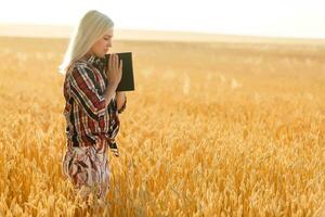 Christian Frau beten auf heilig Bibel und hölzern Kreuz im Gerste Feld auf Sommer. Frau beten zum Gott Segen zu wünsche haben ein besser Leben und glauben im Güte. foto