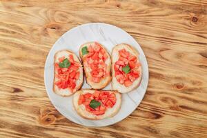 köstlich Bruschetta, getoastet Brot mit Tomaten auf ein Platte, auf ein hölzern Hintergrund, oben Aussicht foto