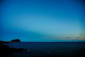 ein Blau Himmel Über das Ozean mit ein klein Insel im das Entfernung foto