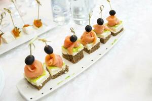 Buffet Gerichte.Häppchen auf ein Weiß Platte. klein Sandwiches auf ein Stock. Snack von schwarz brot, Lachs und Salat foto