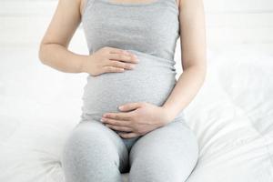 Nahaufnahme einer schwangeren Frau, die auf dem Bett sitzt und zu Hause ihren Bauch berührt. selektiver Fokus foto