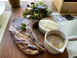 gegrillt oder gebraten Schweinefleisch Koteletts auf das Knochen mit Salat und püriert Kartoffeln serviert auf hölzern Tafel foto