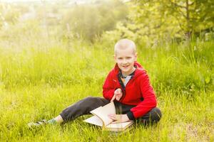 Porträt von ein Junge Sitzung mit ein Buch im das Park foto