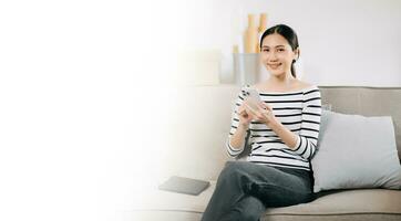jung asiatisch Frau mit Smartphone und Tablette während sitzend auf Couch beim Zuhause foto