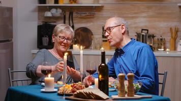 Senior im Ruhestand alt Ehefrau zeigen Fotos auf Smartphone zu ihr Mann während romantisch Abendessen. Paar Sitzung beim das Tisch, reden, mit das Telefon, feiern ihr Jahrestag im das Essen Zimmer.
