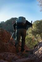 mittleren Alters Mann klettert das Berg im das garraf natürlich Park, unterstützt durch Wandern Stangen. foto