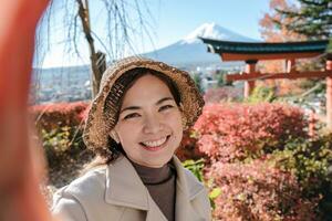heiter asiatisch weiblich Tourist tragen ein Hut nimmt ein Selfie im das Hintergrund im Japan foto