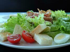 Salat mit Kopfsalat, Schinken, Ei, Croutons und Tomate auf ein Teller schließen oben foto