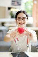 medizinisch Schüler Aktion halten und geben ein Gummi rot Herz auf verschwommen Hintergrund. asiatisch medizinisch Schüler mit Herz Krankheit Konzept. foto