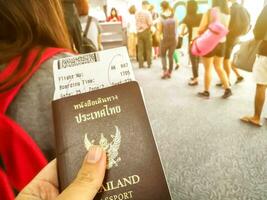 Bangkok Stadt, 2018 -Hand von thailändisch Bürger halten das Thailand Reisepass mit Flugzeug Einsteigen bestehen und Linie oben zu prüfen im Fluggesellschaft Zähler auf verschwommen viele Touristen und Sonne Fackel im Flughafen. foto