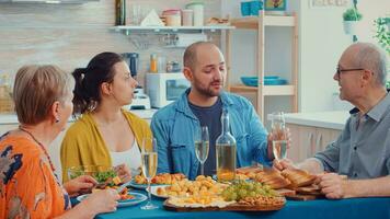 Männer klirren und diskutieren während das Abendessen. multi Generation, vier Menschen, zwei glücklich Paare reden und Essen während ein Gourmet Mahlzeit, genießen Zeit beim heim, im das Küche Sitzung durch das Tisch. foto