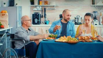 immobilisiert Senior Mann feiern mit Familie haben Abendessen. zwei glücklich Paare reden, lächelnd und Essen während ein Gourmet Mahlzeit, genießen Zeit beim Zuhause Sitzung um das Tabelle im das Küche. foto