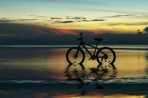 Silhouette von ein Fahrrad auf ein See beim Dämmerung. foto