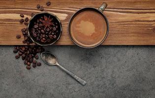 geröstete Kaffeebohnen mit Kaffeetasse auf dunklem Steinhintergrund.