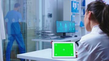 Chroma Schlüssel auf Tablette pc Anzeige benutzt durch Arzt im Krankenhaus Kabinett und Krankenschwester Verlassen das Klinik tragen Blau Uniform. Arzt im Gesundheit Klinik Arbeiten auf Tablette Computer mit austauschbar Bildschirm tun Medizin Forschung. foto