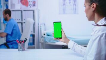 Medizin im Weiß Mantel halten Smartphone mit Grün Bildschirm im Krankenhaus Kabinett. Krankenschwester tragen medizinisch Blau Uniform. foto