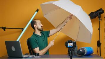 Fotograf halten Weiß Regenschirm zum Blitz im Studio während Aufzeichnung vlog. Fachmann Studio Video und Foto Ausrüstung Technologie zum arbeiten, Foto Studio Sozial Medien Star und Influencer