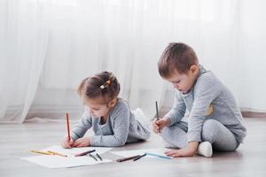 Kinder liegen im Schlafanzug auf dem Boden und zeichnen mit Bleistiften. süßes Kind malen mit Bleistiften foto