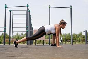 glückliche Frau, die an sonnigen Sommertagen auf dem Sportplatz trainiert und ihre Beine streckt foto