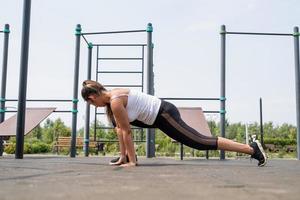 glückliche Frau, die an sonnigen Sommertagen auf dem Sportplatz trainiert und ihre Beine streckt foto