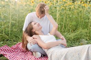 junges Paar beim Picknick auf Sonnenblumenfeld bei Sonnenuntergang