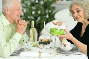 Alten Paar beim das Abendessen Tabelle geben ein Neu Jahre Geschenk foto