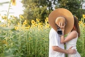 junges glückliches Paar, das sich auf einer Picknickdecke küsst und ihre Gesichter mit einem Sommerhut bedeckt foto