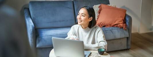 Arbeit von heim, freiberuflich und E-Learning Konzept. jung Frau studieren, Sitzung im Vorderseite von Laptop, Arbeiten auf Fernbedienung, Arbeitsplatz im Leben Zimmer foto