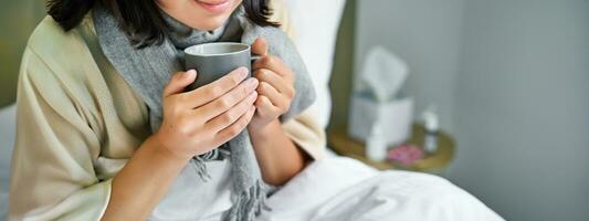 schließen oben von weiblich Hände halten heiß trinken, Lügen im Bett, Mädchen fangen ein kalt und bleiben beim Zuhause foto