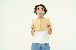 süß Brünette Mädchen, spielen mit Stift, halten Bleistift mit ihr Lippe, halten Planer, Schreiben im Tagebuch, posieren Über Weiß Studio Hintergrund foto