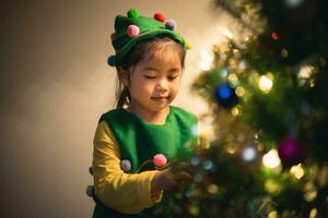 Kinder Kinder Mädchen hängend ein klein funkeln Ball dekorieren Weihnachten Baum zum feiern Weihnachten und Neu Jahr Party beim heim. vorbereiten zum Urlaub. Glück Weihnachten Tag. haben Spaß. Weihnachten Konzept. foto