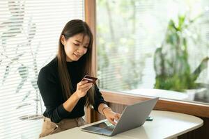 Frau halten Anerkennung Karte und mit Handy, Mobiltelefon zu Einkaufen online. asiatisch Frau tragen Brille Arbeiten beim heim. online Einkaufen, E-Commerce, Internet Banken, Ausgaben Geld, Arbeiten von Zuhause Konzept. foto