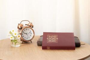 Bibel und Notizbuch auf dem Tisch mit einem Wecker am Fenster. Zeit für das Lernen des Bibelkonzepts foto