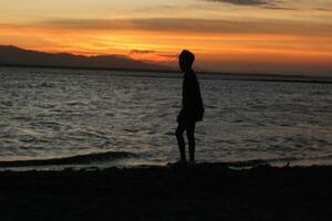 Silhouette eines jungen Mannes, der am See steht und den Sonnenuntergang genießt. friedliche Atmosphäre in der Natur foto