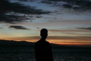Silhouette eines jungen Mannes, der am See steht und den Sonnenuntergang genießt. friedliche Atmosphäre in der Natur foto