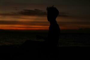 Silhouette eines jungen Mannes, der am See steht und den Sonnenuntergang genießt. friedliche Atmosphäre in der Natur foto