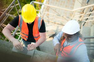 männlich und weiblich Ingenieure Arbeiten auf Konstruktion Grundstück, Sie sind inspizieren das Zement Gips Arbeit auf das Wände und Balkone von das Gebäude. foto