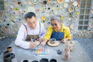 im das Keramik Werkstatt, ein asiatisch im Ruhestand Paar ist beschäftigt, verlobt im Keramik Herstellung und Lehm Gemälde Aktivitäten. foto
