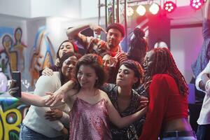 Gruppe von freunde posieren zum Selfie auf überfüllt Nachtclub Tanzfläche während Clubbing zusammen. jung sorglos Menschen nehmen Foto auf Smartphone während genießen Diskothek Veranstaltung