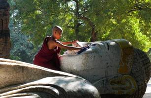 asiatischer Anfängermönch sauber liegende Buddha-Statue außerhalb des Tempels foto