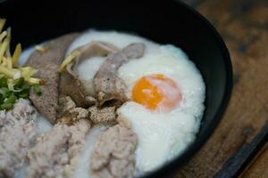 Reisbrei mit Sanft gekocht Ei und Schweinefleisch Eingeweide im das schwarz Schüssel zum köstlich Frühstück. foto